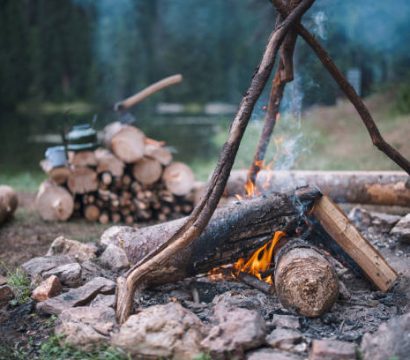 Photo of a campfire in a campsite with wood material and a vintage ax and teapot